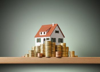 Miniature model house standing on a stack of coins.