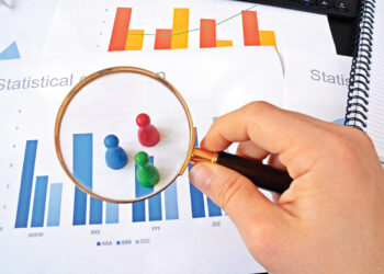 A young man is holding a magnifying glass in his hand, looking at statistic figures - a business concept on the subject of sampling and selecting the right target group and examining it