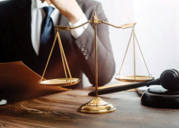 Business and lawyers discussing contract papers with brass scale on desk in office. Law, legal services, advice, justice and law concept picture with film grain effect